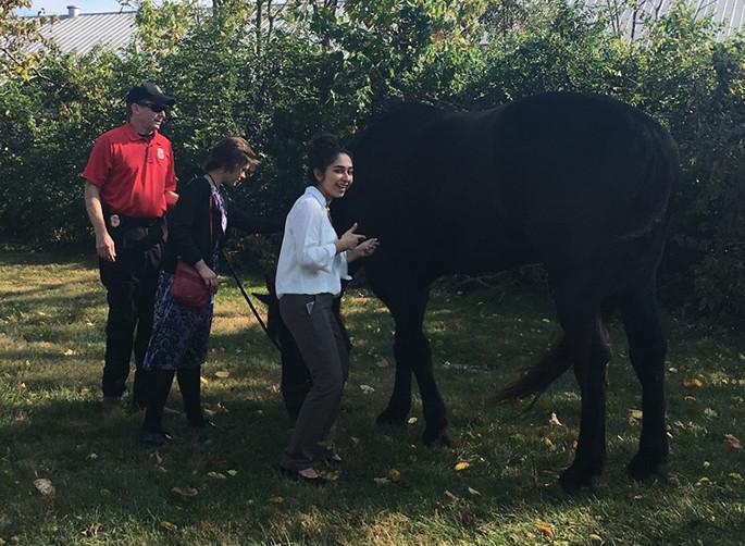 Dunbar LLYP member, Flor Mucino, strikes a pose next to a black firemans thoroughbred, showing the enormity of the horse, as part of the Health and Human Services Day.