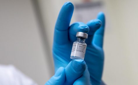 Vial of COVID-19 vaccine in a gloved hand.